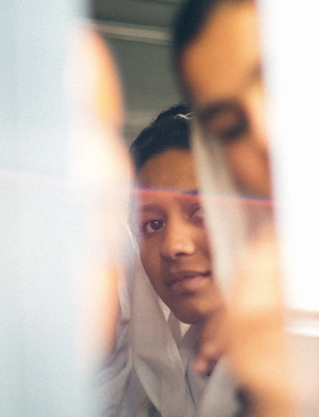 Close-up of a young woman looking through a narrow gap with a soft focus on surrounding faces.
