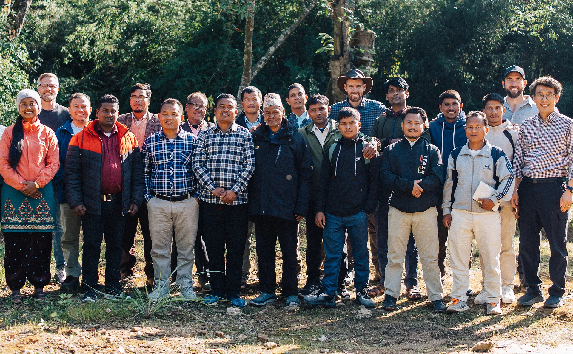 Group of diverse people standing outdoors on a sunny day with trees in the background.