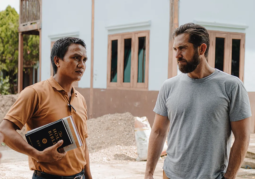 Two men engaged in a serious conversation outside, one holding a Bible and a notebook.
