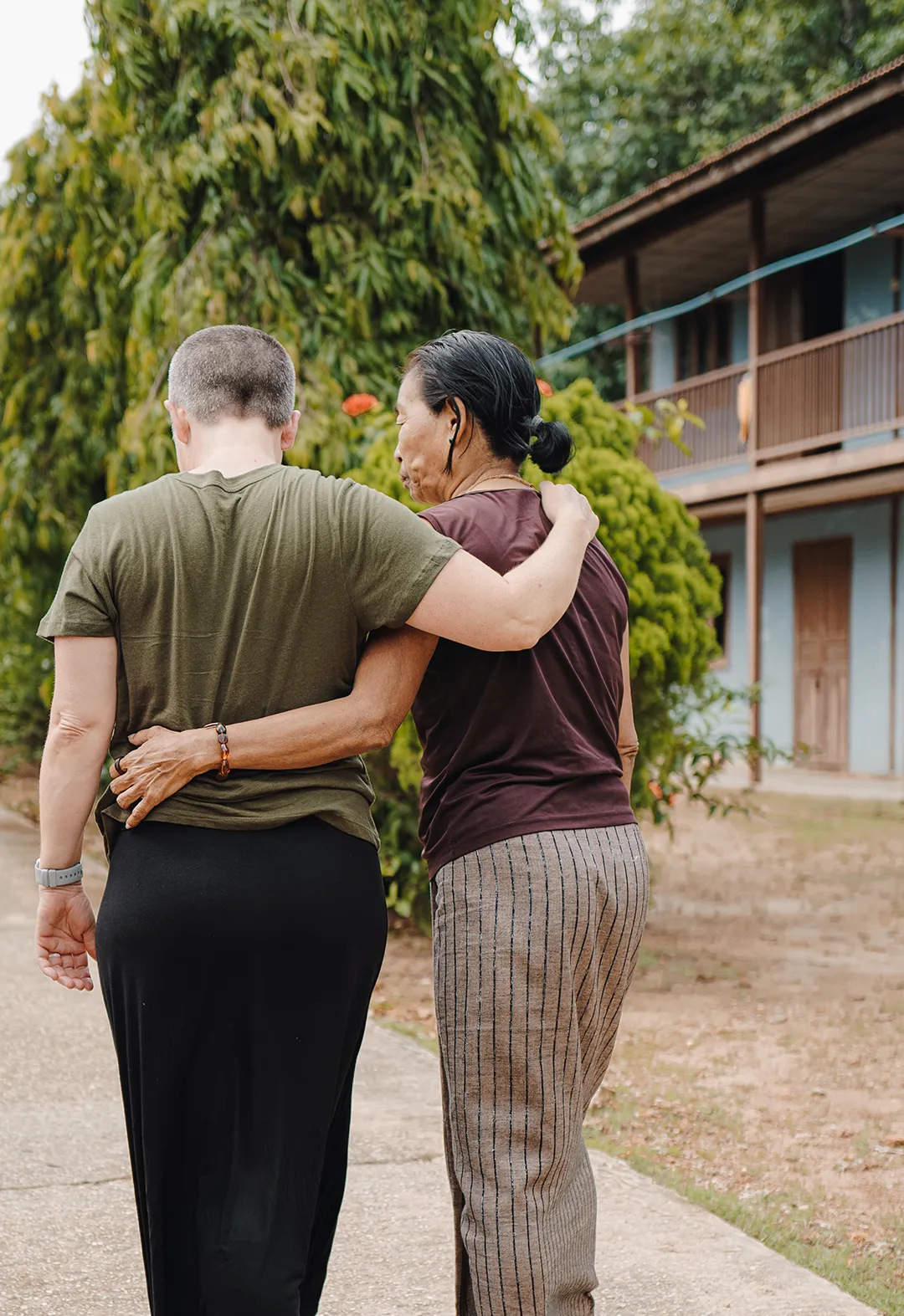 Two women walking arm in arm outdoors near a building, showing support and friendship.