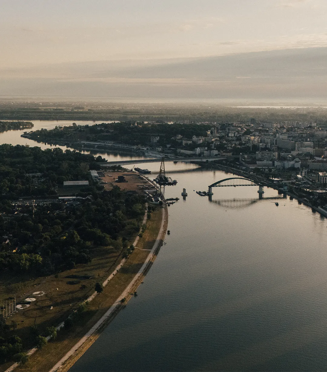 Aerial view of a river flowing through a city with bridges and green areas on the banks during sunset.