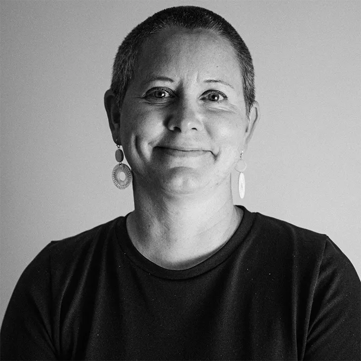 Black and white portrait of a smiling person with short hair and circular earrings wearing a dark shirt against a plain background.