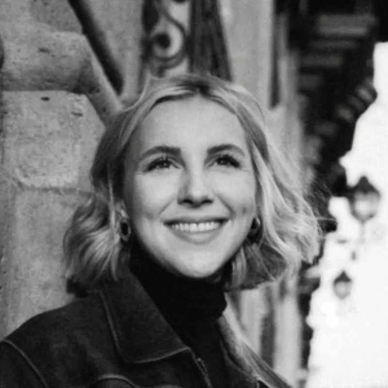 Black and white portrait of a smiling young woman with medium-length wavy hair wearing a dark jacket and hoop earrings.