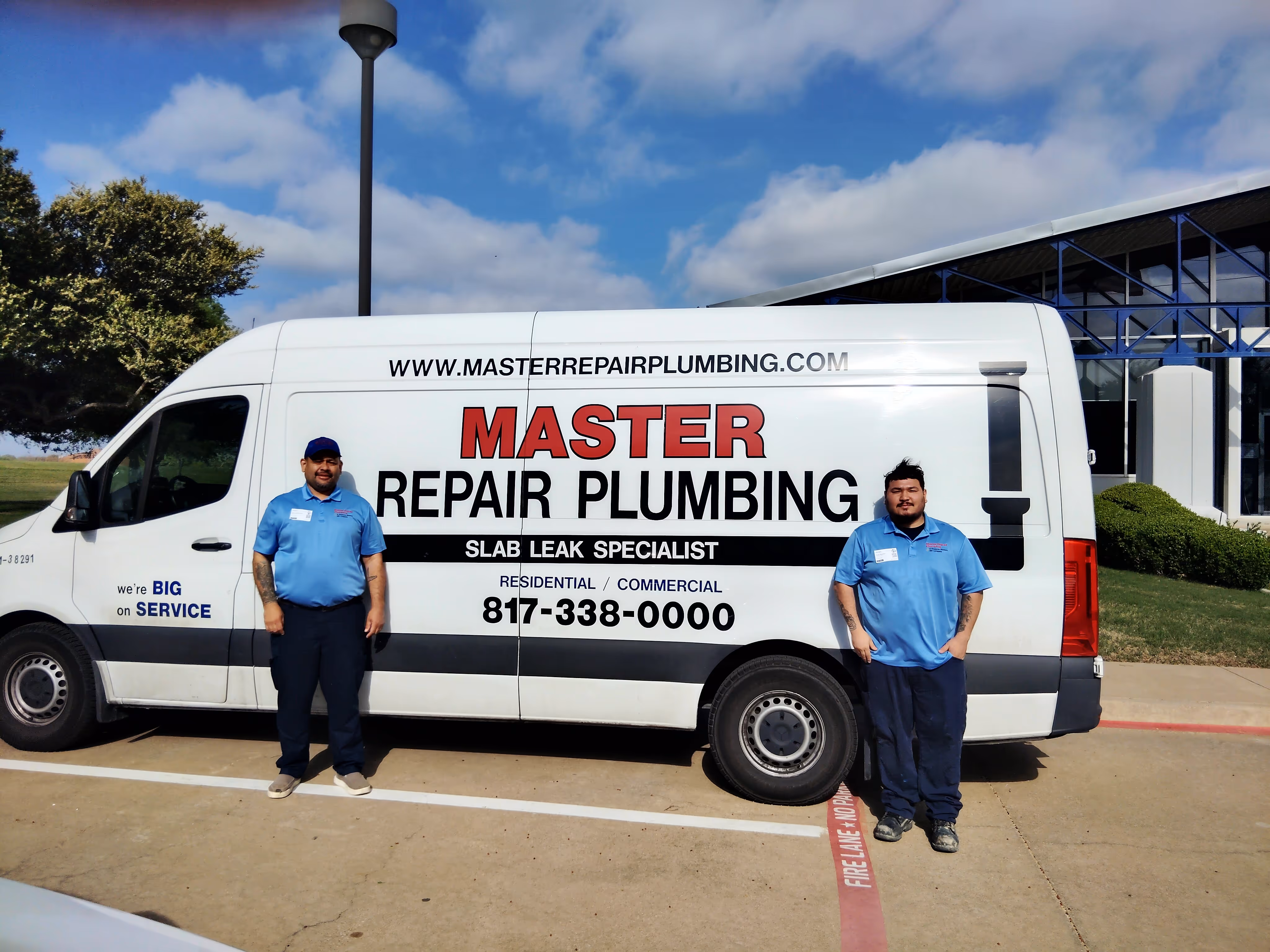 Two men in blue uniforms standing in front of a white Master Repair Plumbing van with company contact details and services listed.
