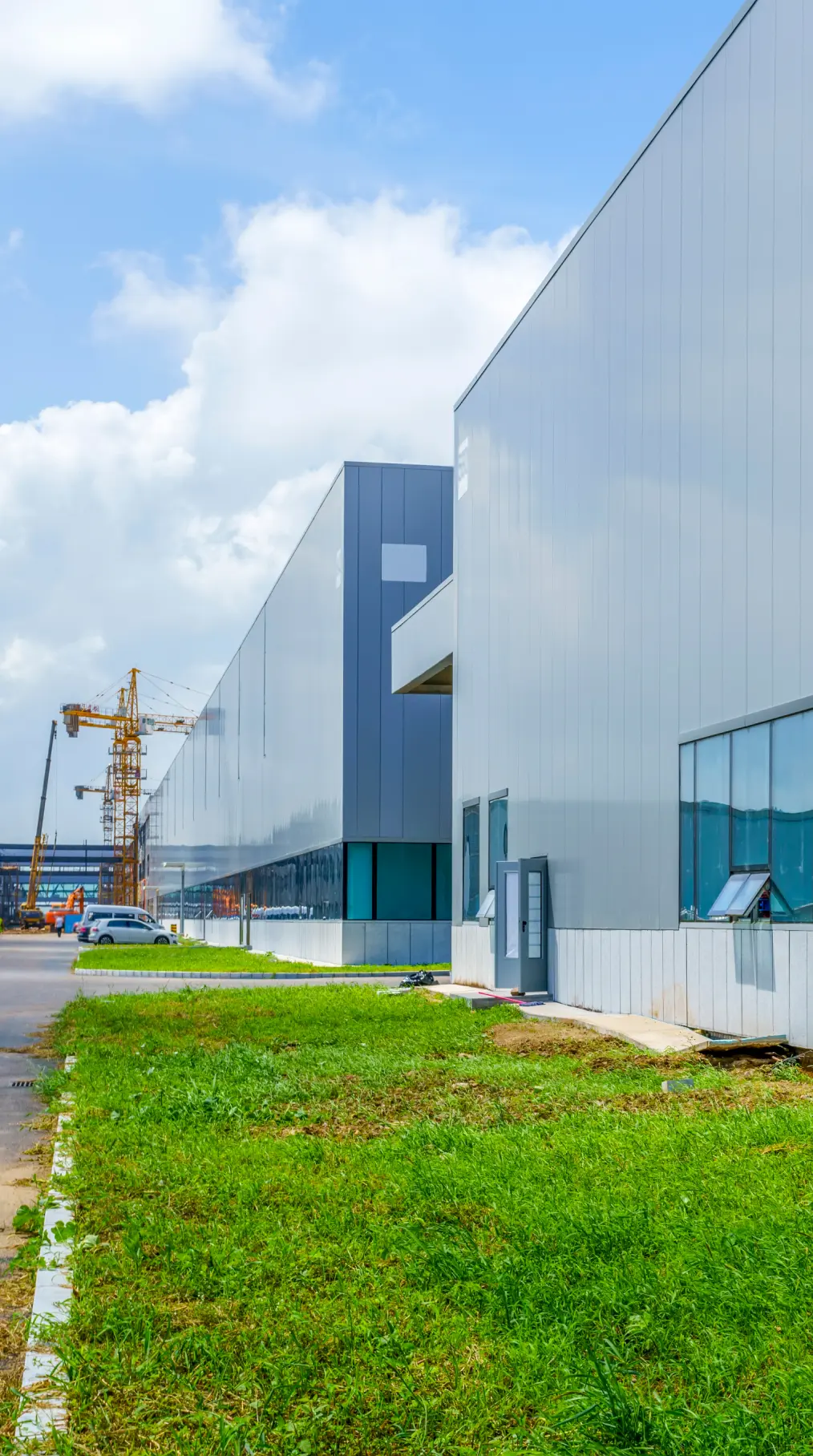 Modern industrial warehouse buildings with reflective glass windows and construction cranes in the background.