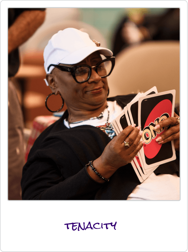 Woman in glasses and white cap holding UNO cards with a focused expression.