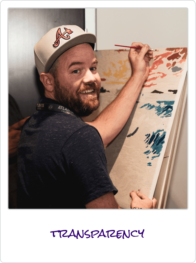 Smiling man in Atlanta baseball cap painting on a canvas with bright colors.