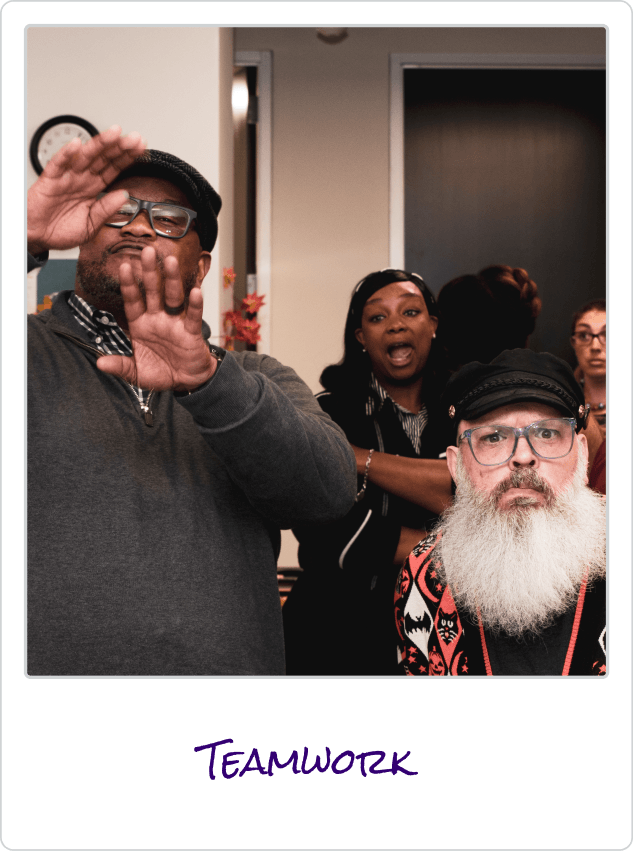 Four diverse coworkers in a meeting room displaying engagement and emotion, with word Teamwork below.