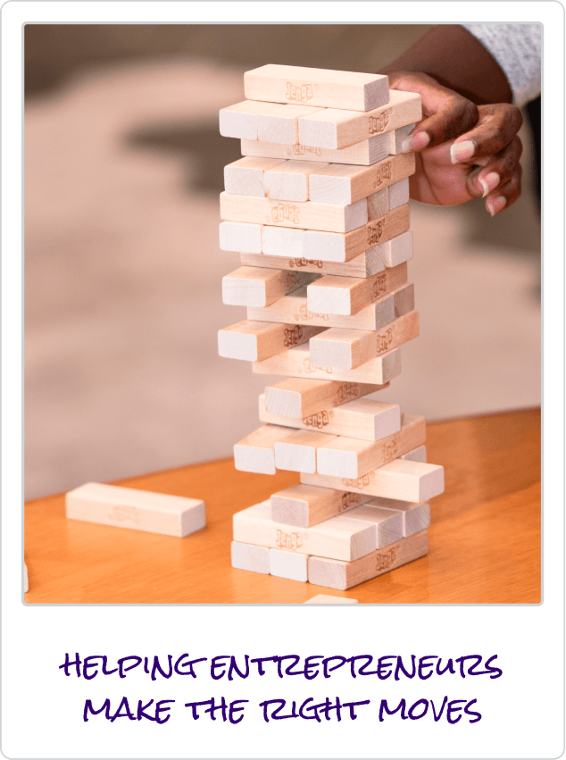 Person's hand carefully removing a block from a Jenga tower on a wooden table.