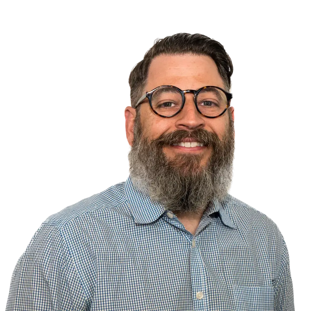 Smiling man with a thick beard, glasses, and a checkered button-up shirt against a transparent background.