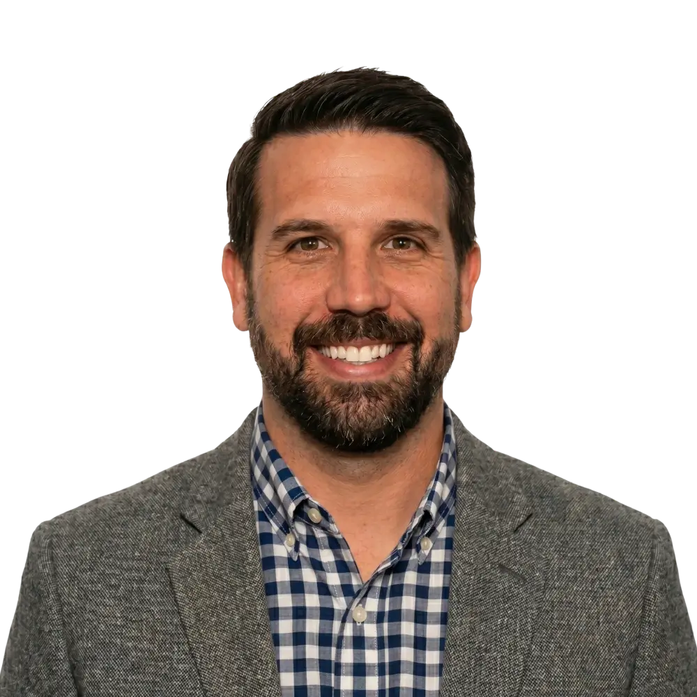 Smiling man with short dark hair and beard wearing a gray blazer and blue checkered shirt.