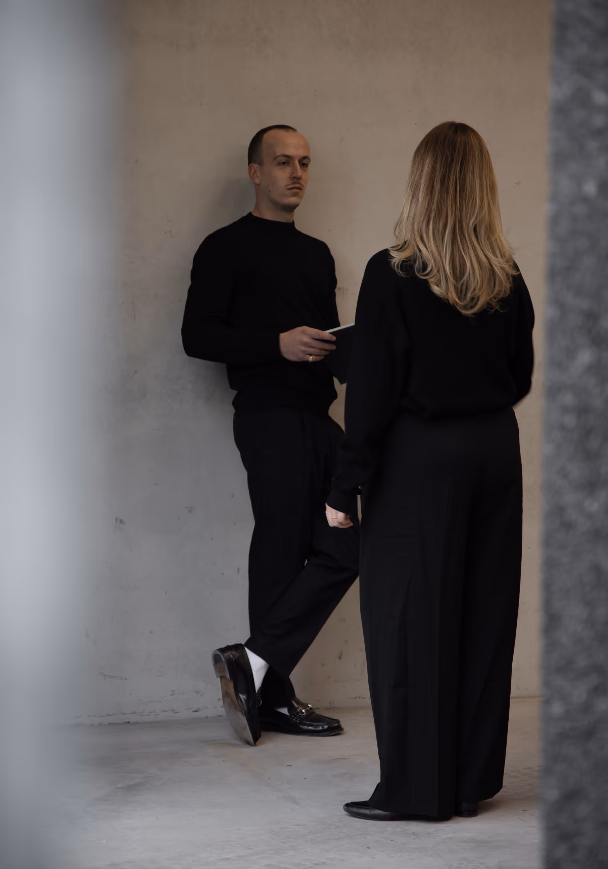 Olivier en Gaëlle gekleed in zwarte kleding staan binnen en praten, de man houdt een tablet vast.