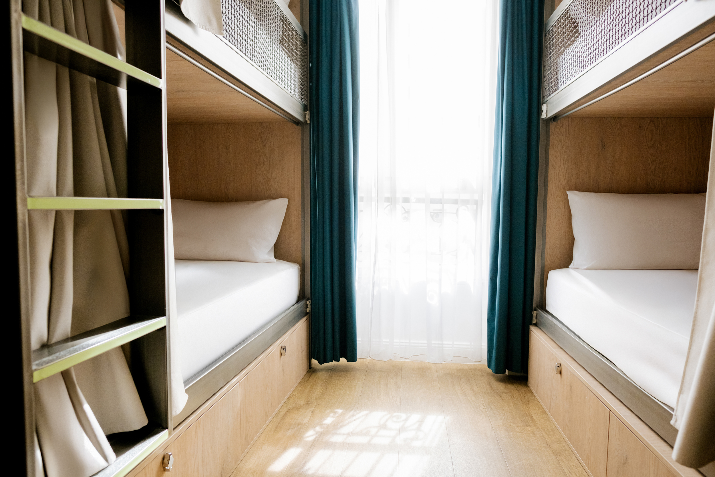 Chambre avec lits superposés en bois, rideaux bleus, grande fenêtre avec voilage blanc.