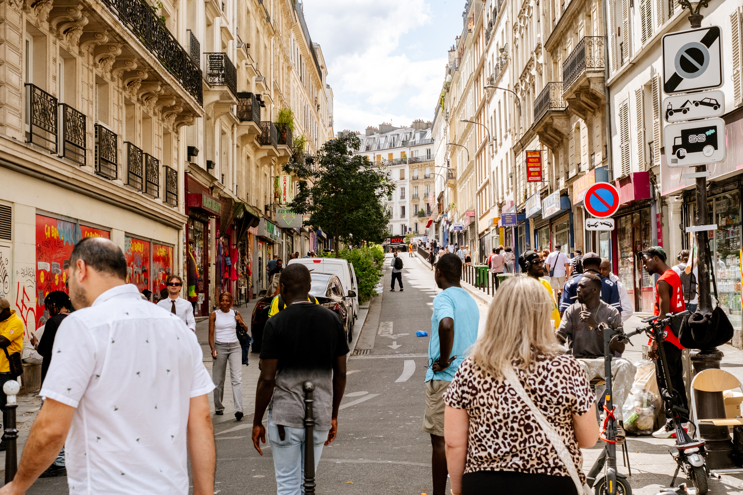 Rue animée à Paris avec des passants marchant entre des immeubles et des boutiques colorées.