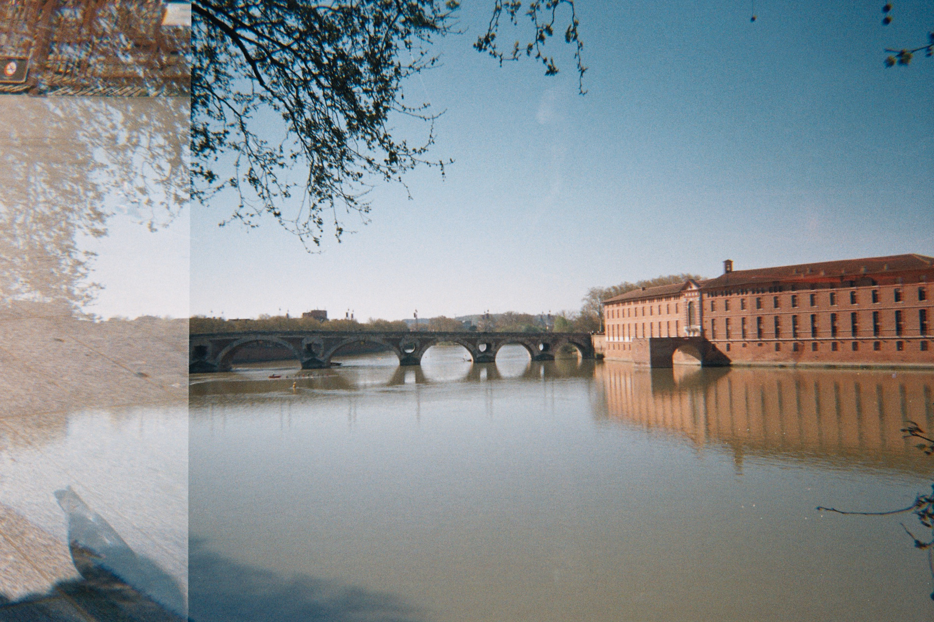 Pont en pierre à plusieurs arches sur une rivière calme avec un grand bâtiment en brique à droite.