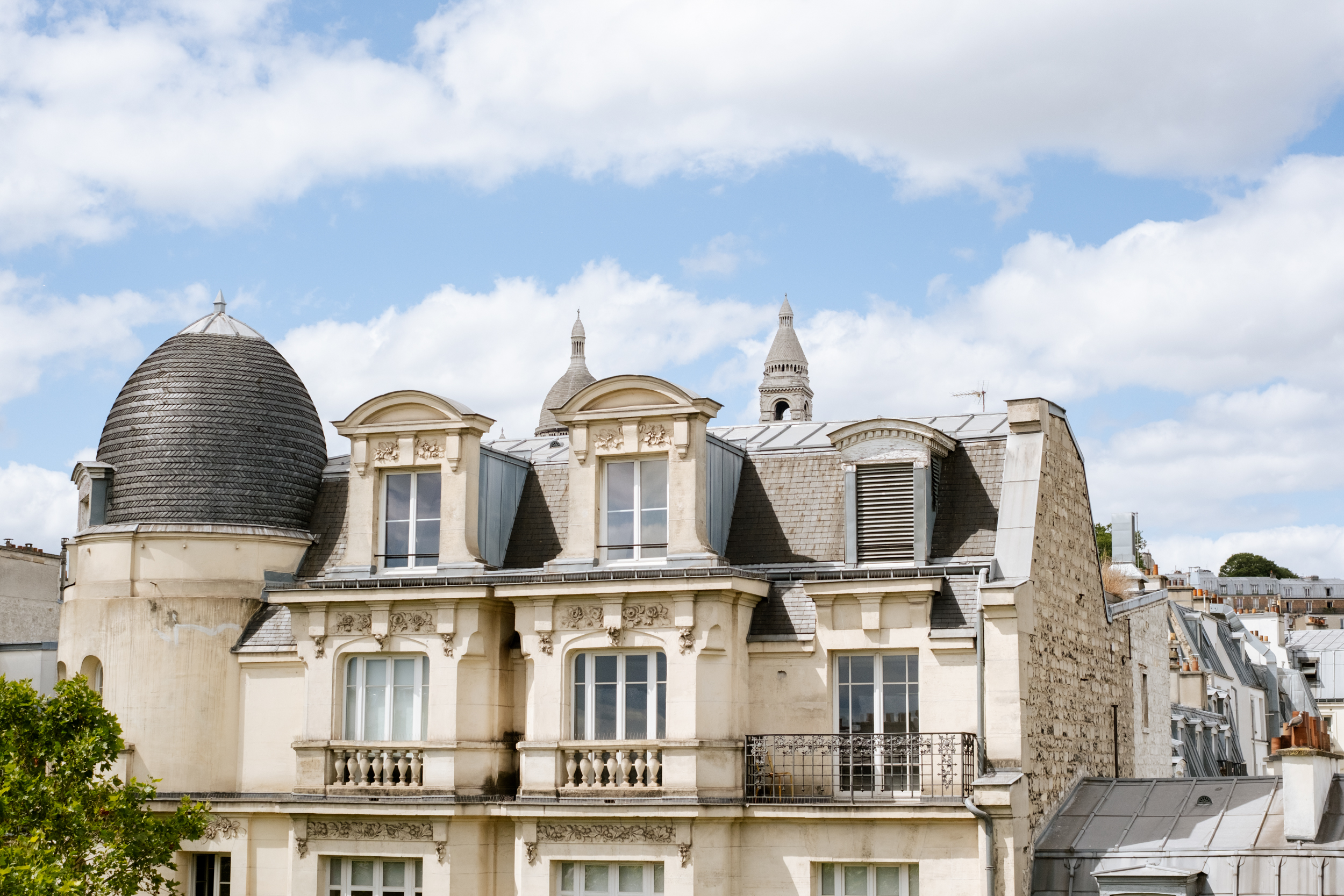 Façade d'un immeuble parisien classique sous un ciel bleu avec des nuages blancs.