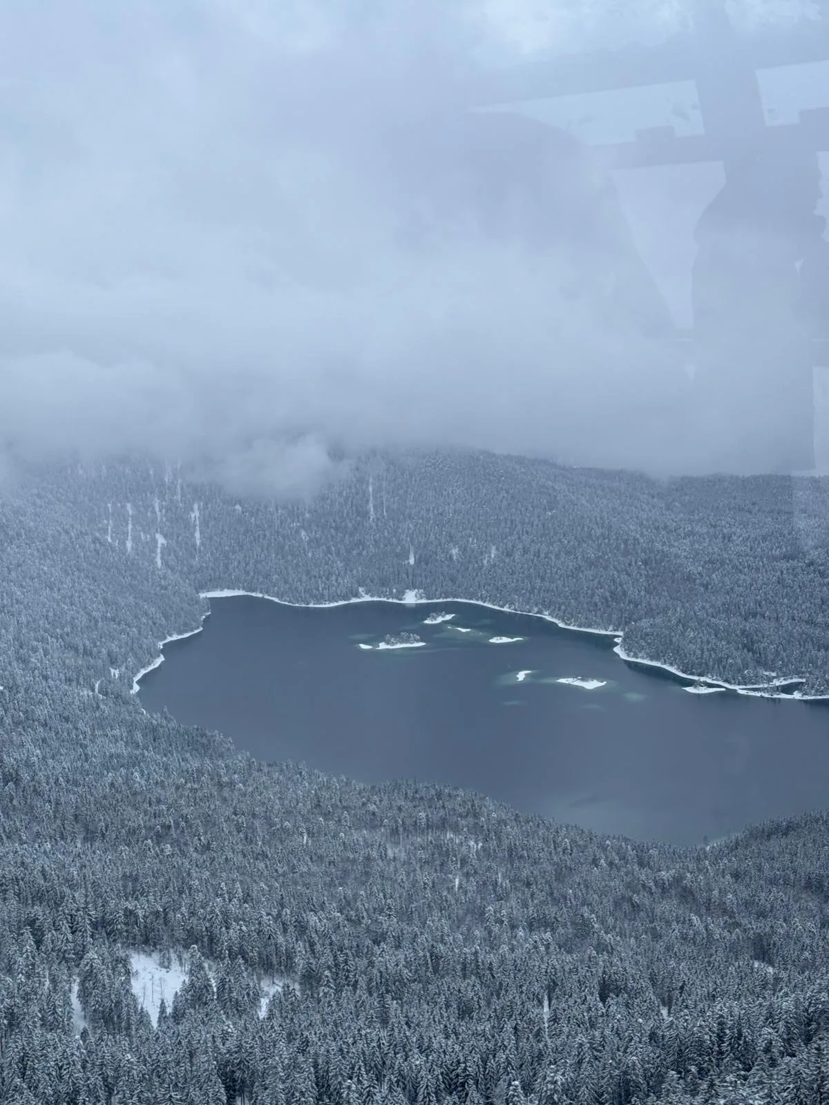 Blick aus der Gondel auf einen verschneiten Bergwald und einen See an der Zugspitze