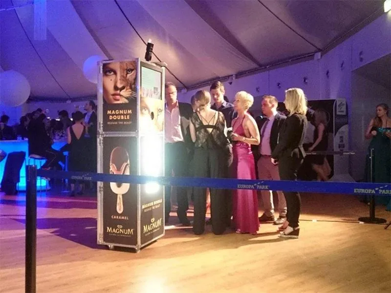 Magnum-Eisstation mit beleuchtetem Display im Festzelt, davor Gäste in Abendgarderobe