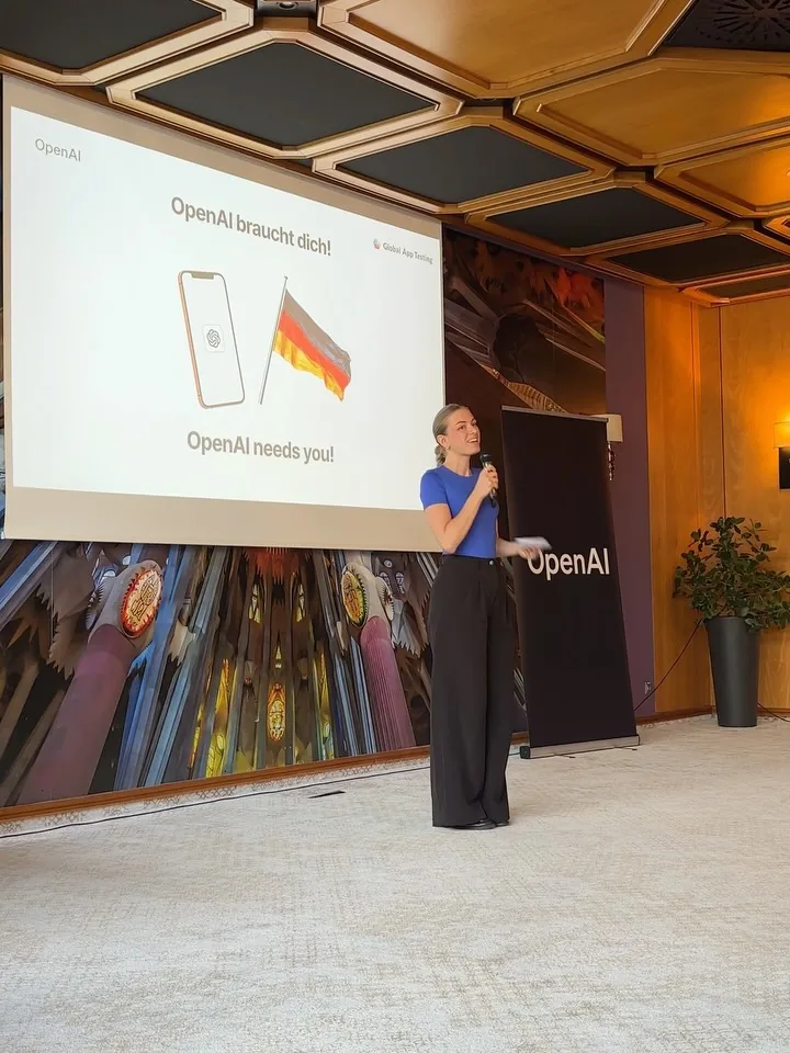 Bühne beim OpenAI Experience Lab mit Projektion „OpenAI braucht dich! OpenAI needs you!“ und Moderatorin Maja Junginger