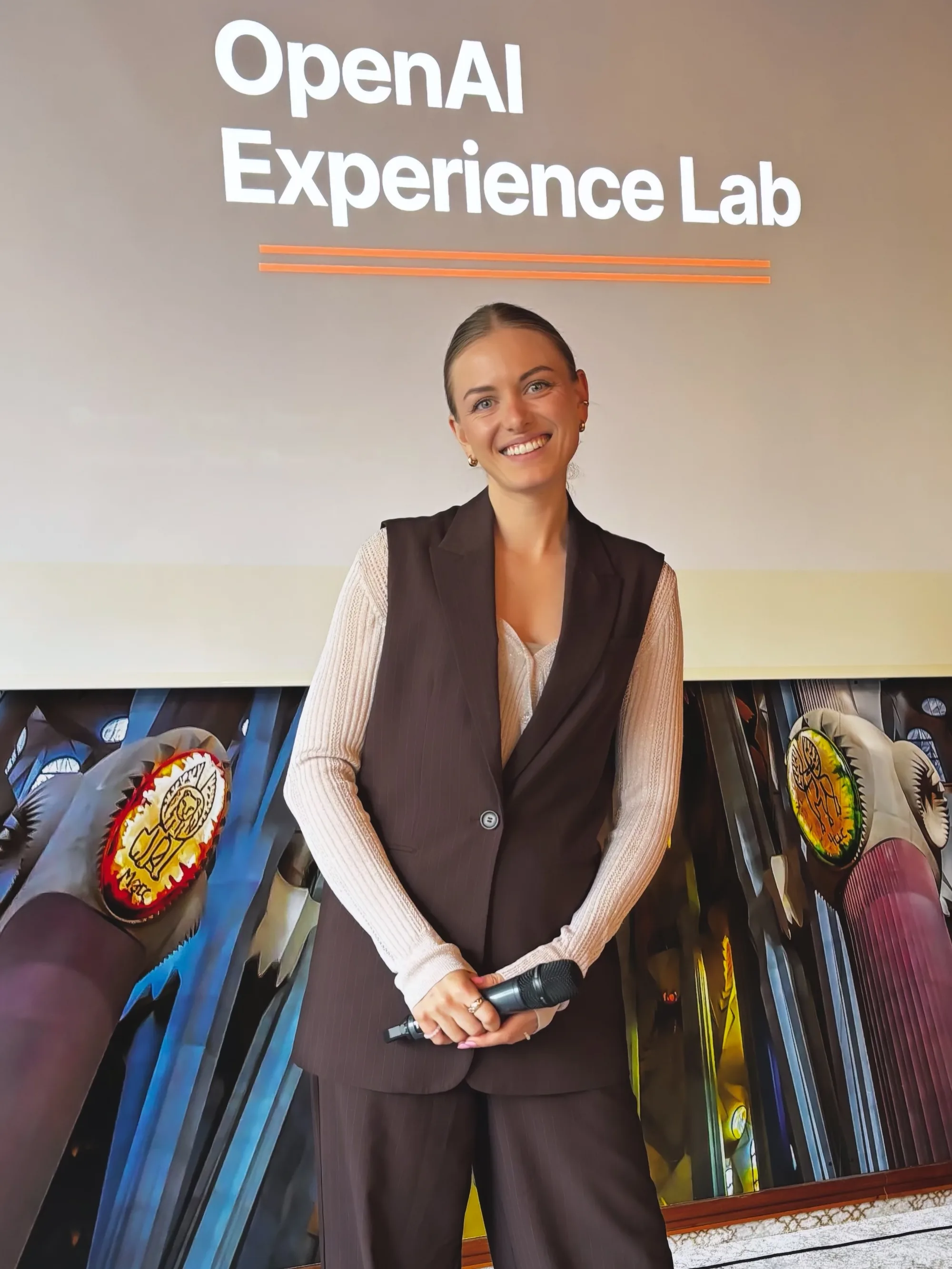 Moderatorin Maja Junginger lächelnd vor der Leinwand mit dem Schriftzug OpenAI Experience Lab