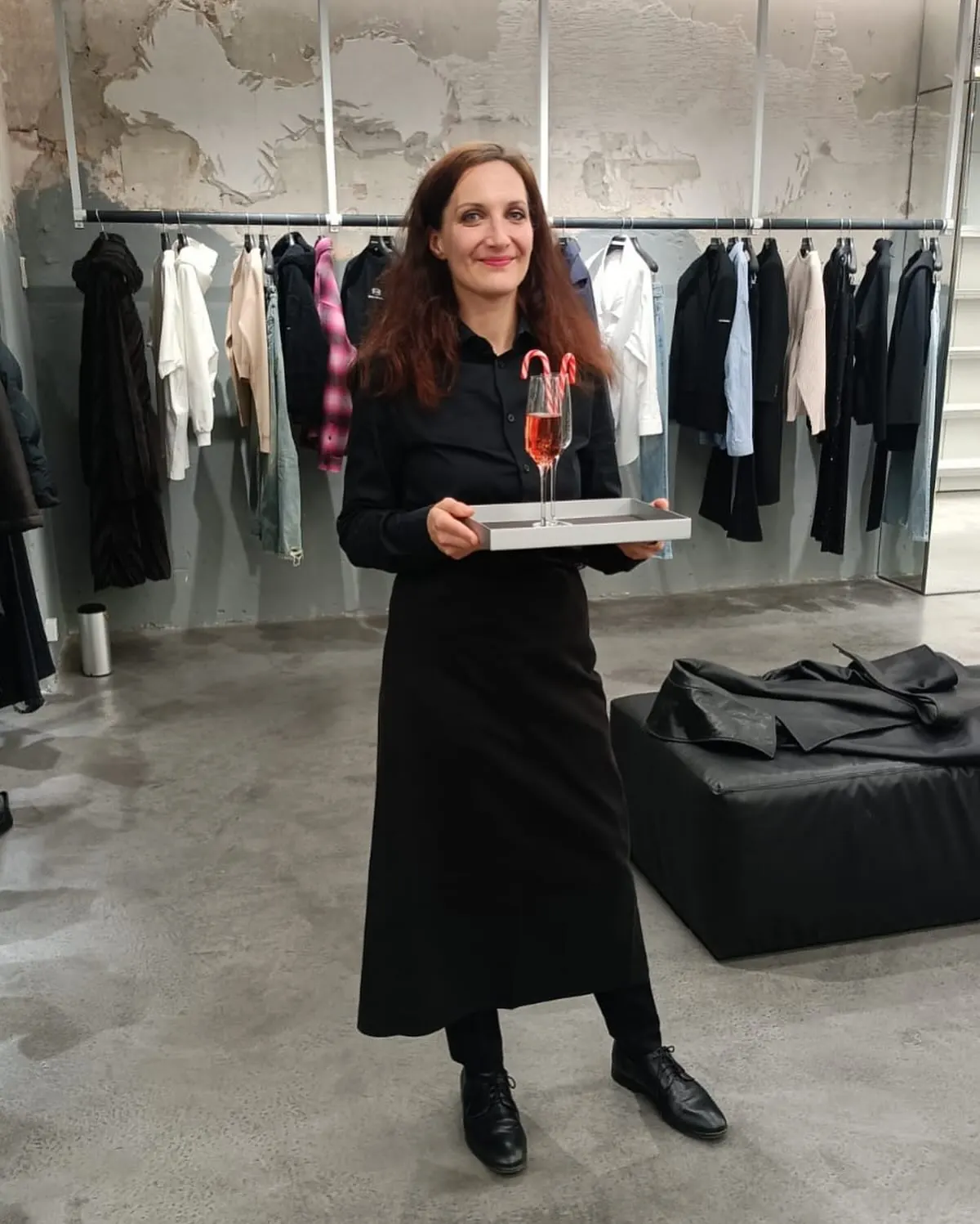 Servicehostess von eventas mit Glas auf dem Tablett vor Kleiderstangen bei einem BALENCIAGA-Einsatz