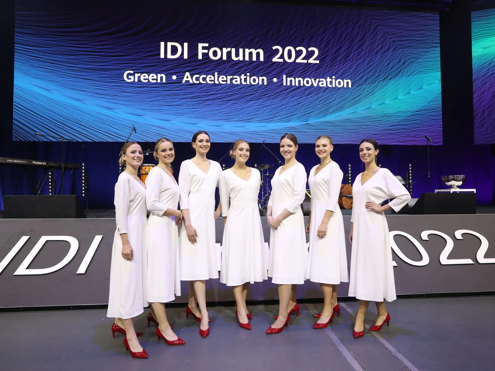 Seven hostesses in white dresses and red shoes in front of the stage of the Huawei IDI Forum 2022 | eventas
