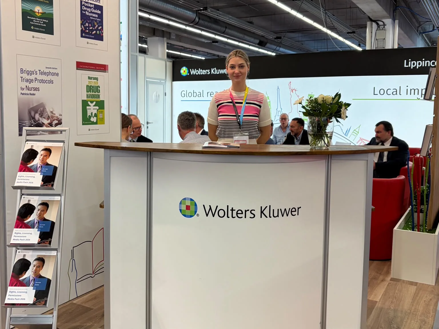Hostess Sophia am Empfangstresen von Wolters Kluwer auf der Frankfurter Buchmesse 2026, dahinter Besprechungstische am Messestand | eventas