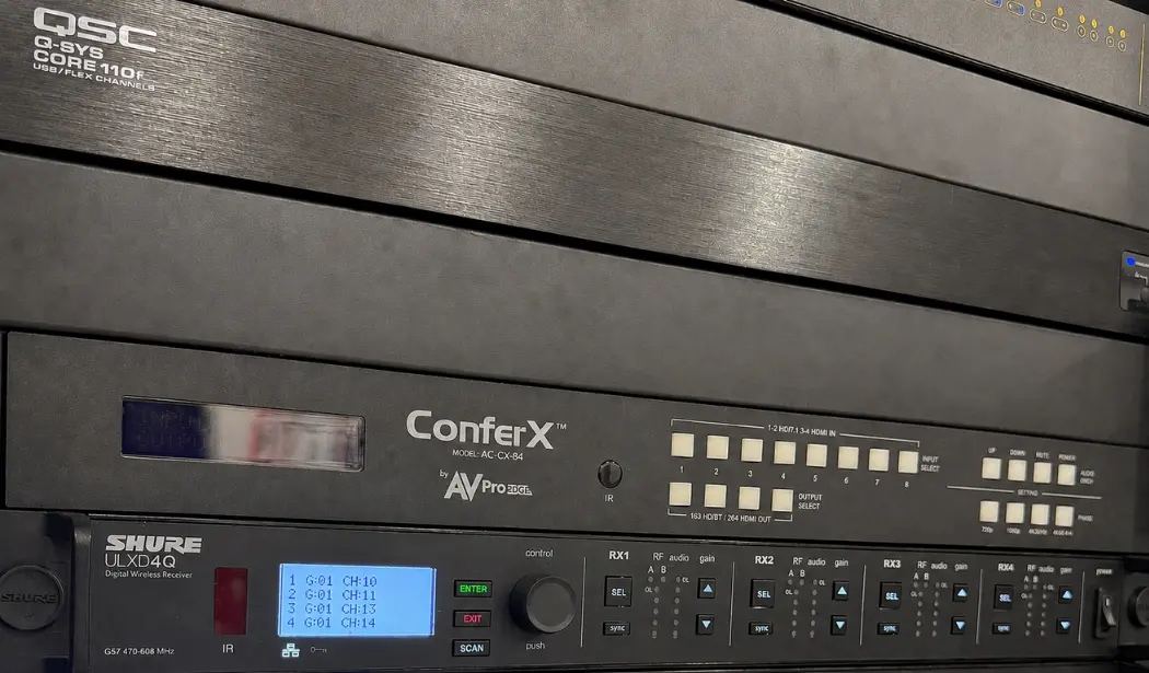 Professional audiovisual equipment rack with digital signal processor, video switching system, and wireless microphone receiver.