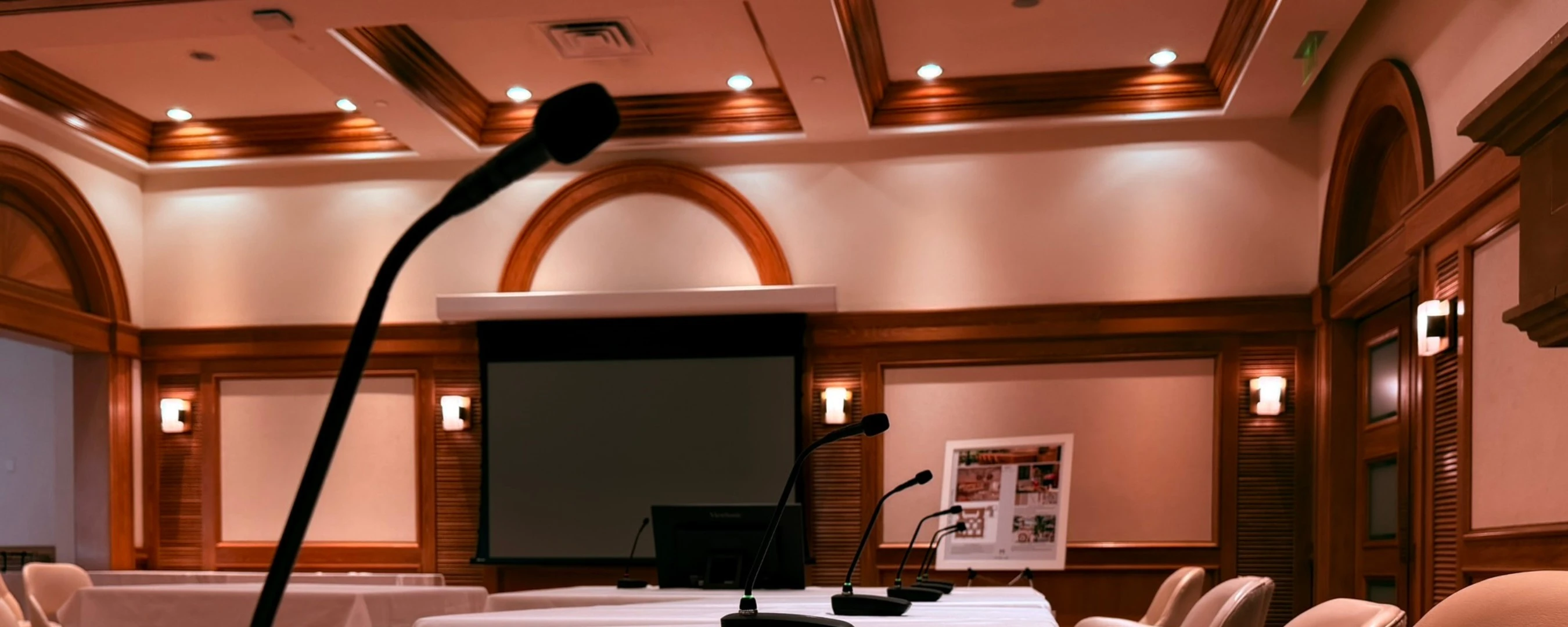 Executive boardroom with wireless tabletop microphones, large projection screen, and premium interior finishes.
