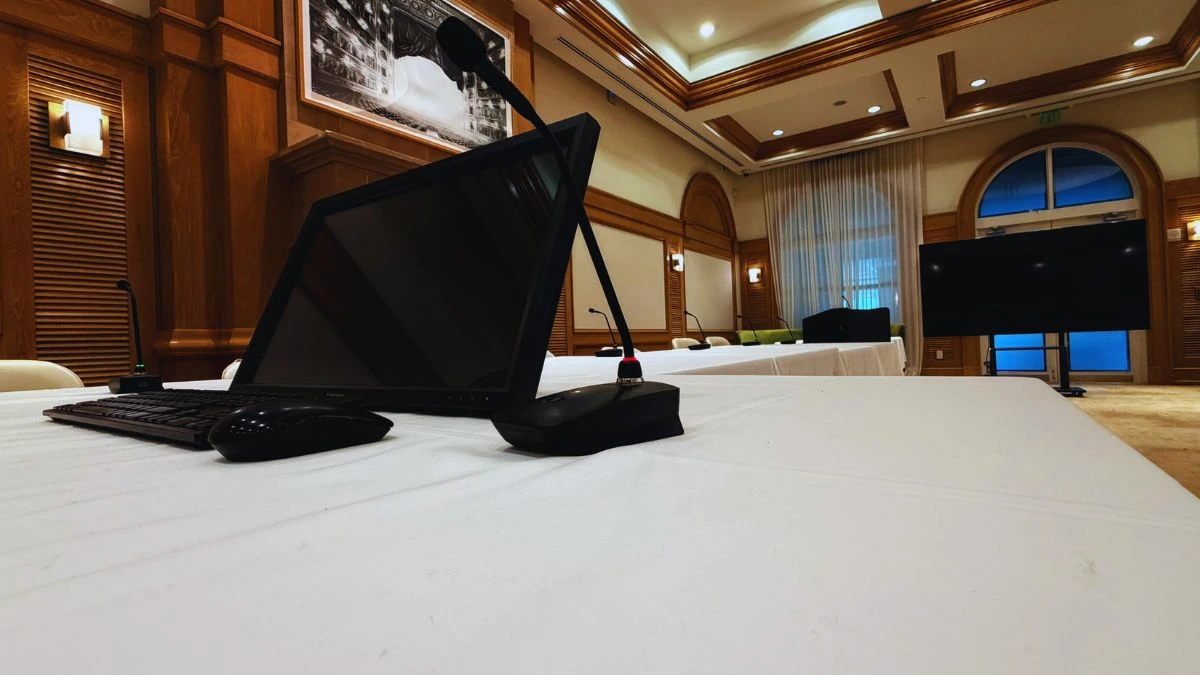 Executive conference room with presenter workstation, wireless tabletop microphones, large presentation display, and premium interior design.  Grade: A+