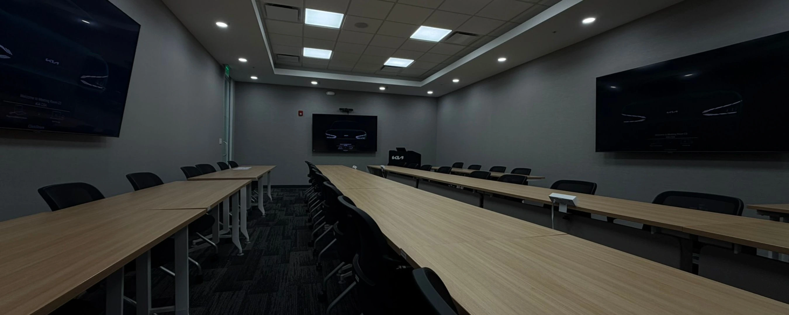 Modern training and conference room with three presentation displays, presenter lectern, and collaborative meeting tables.