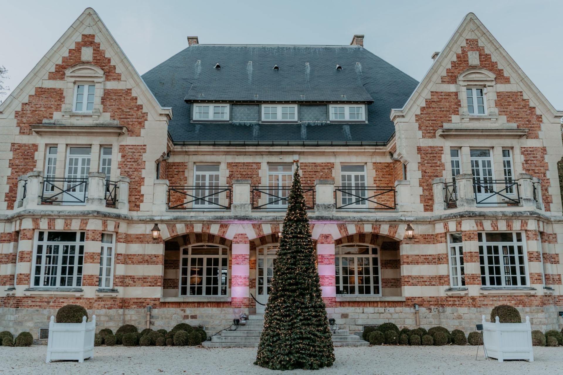 Grande demeure en briques et pierres avec sapin de Noël décoré devant l'entrée