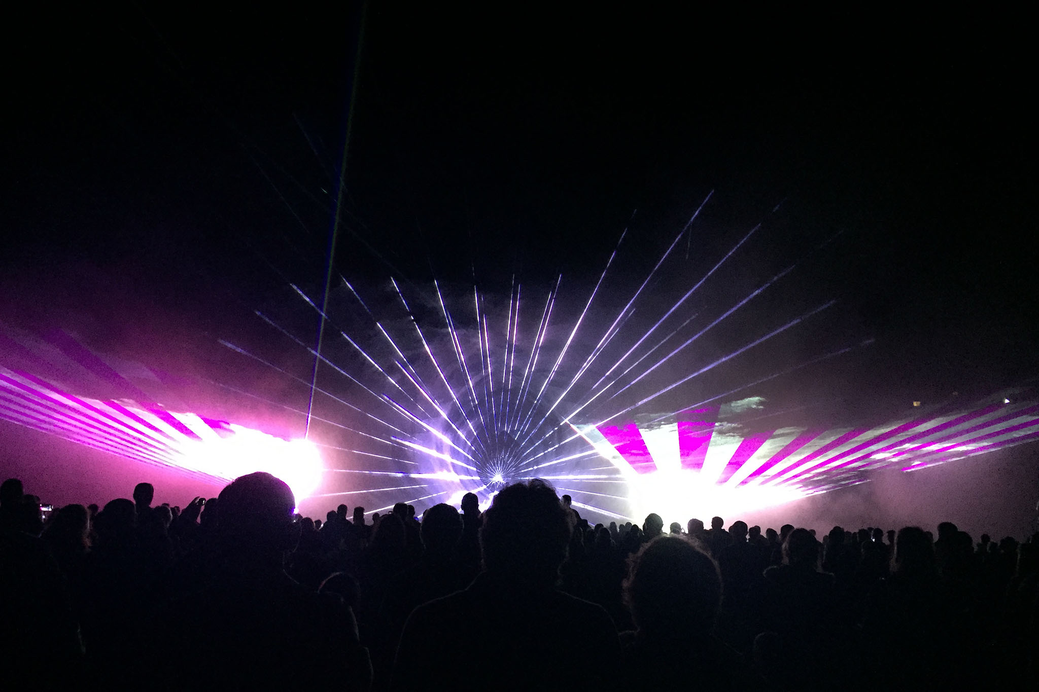 Spectacle de lumières laser violets et blancs rayonnant depuis le centre devant la foule