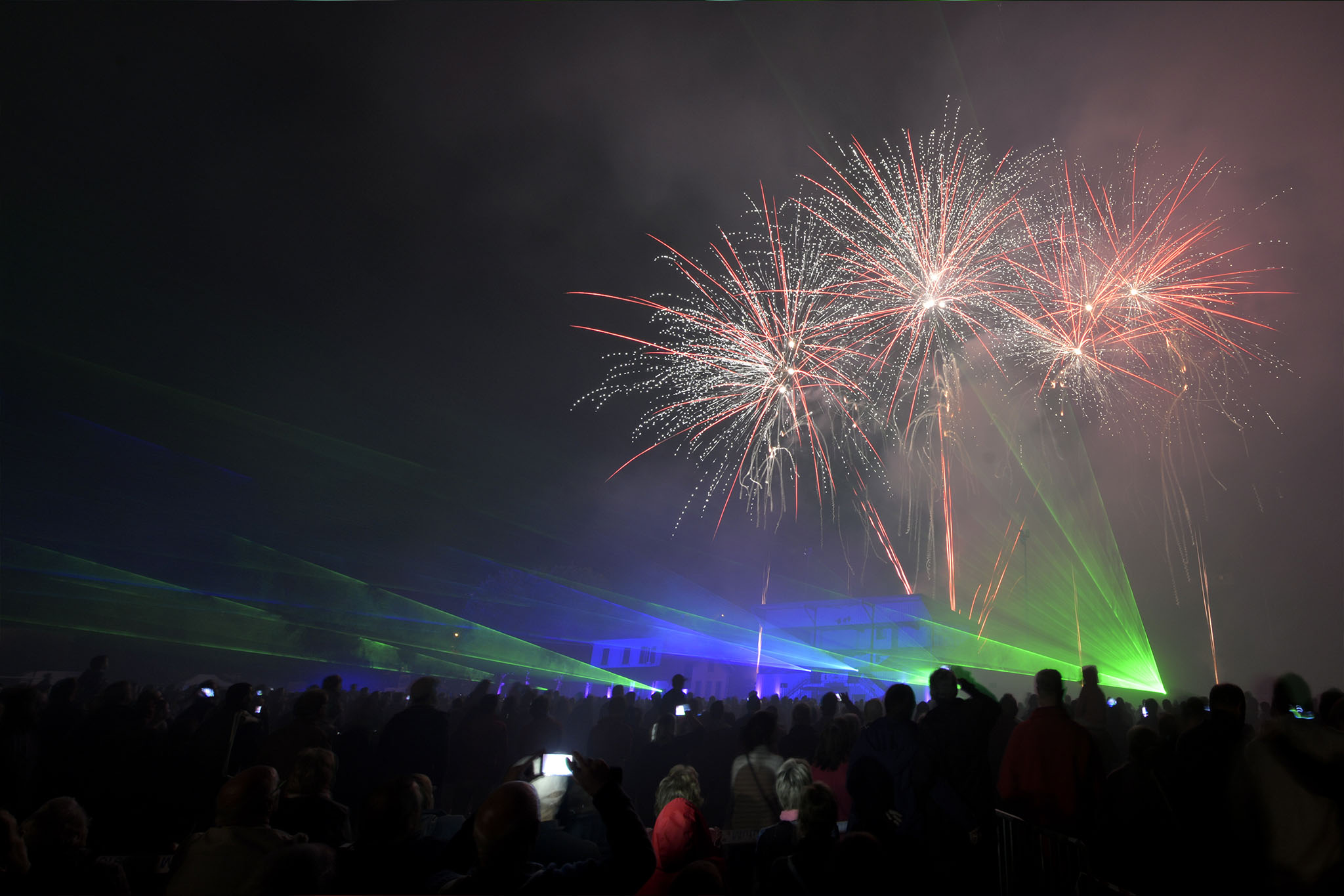 Feu d'artifice nocturne avec projection laser verte sur bâtiment historique devant une foule