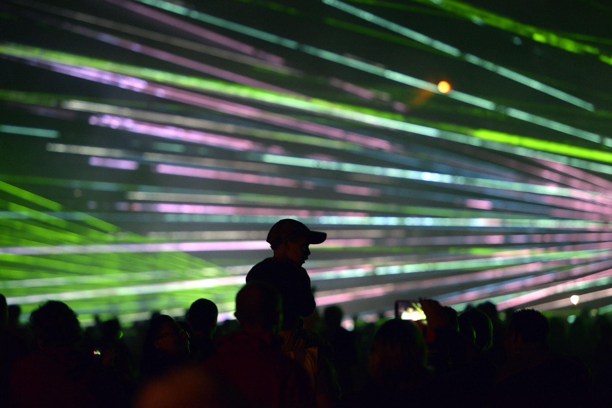 Silhouettes de spectateurs contemplant des faisceaux laser verts et violets dans la nuit