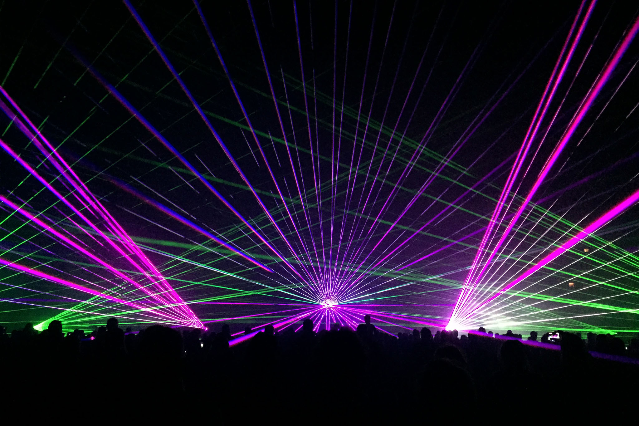 Foule illuminée par des faisceaux laser violets verts et blancs lors des Feux Folies