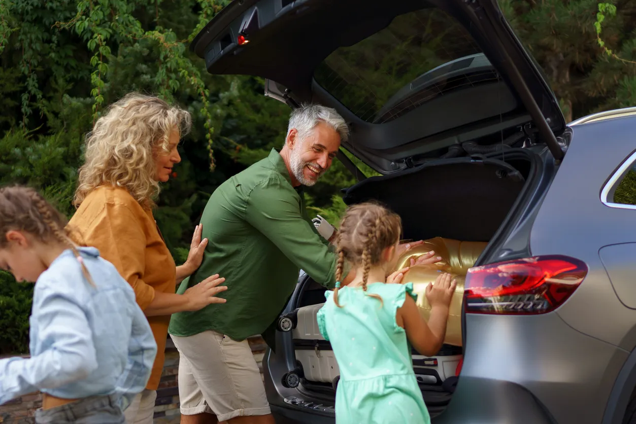 Happy family preparing for holiday, putting suitcases in car trunk, while their electric car charging. stock photo