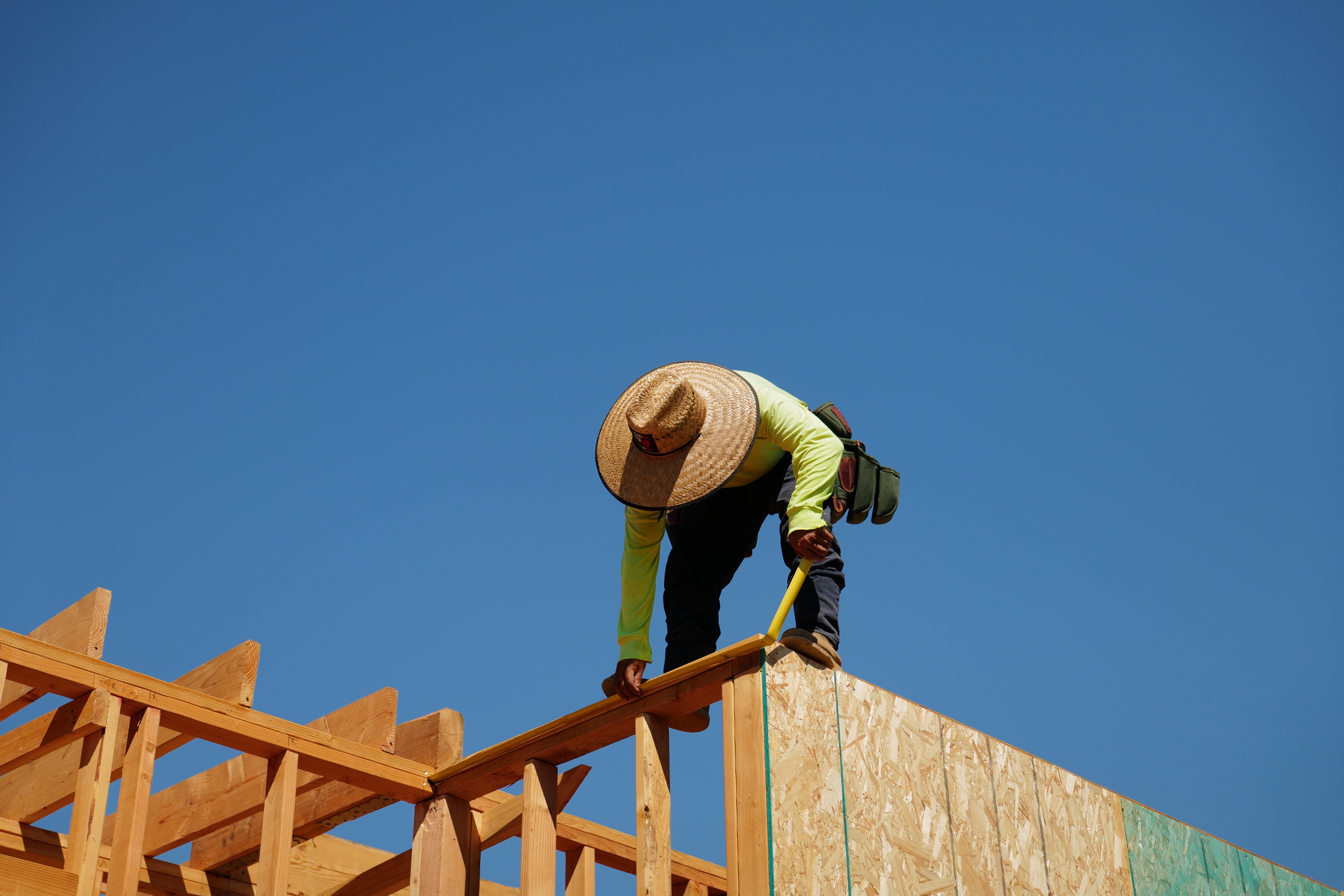 Worker on the roof framing of an Altadena rebuild against a clear blue sky