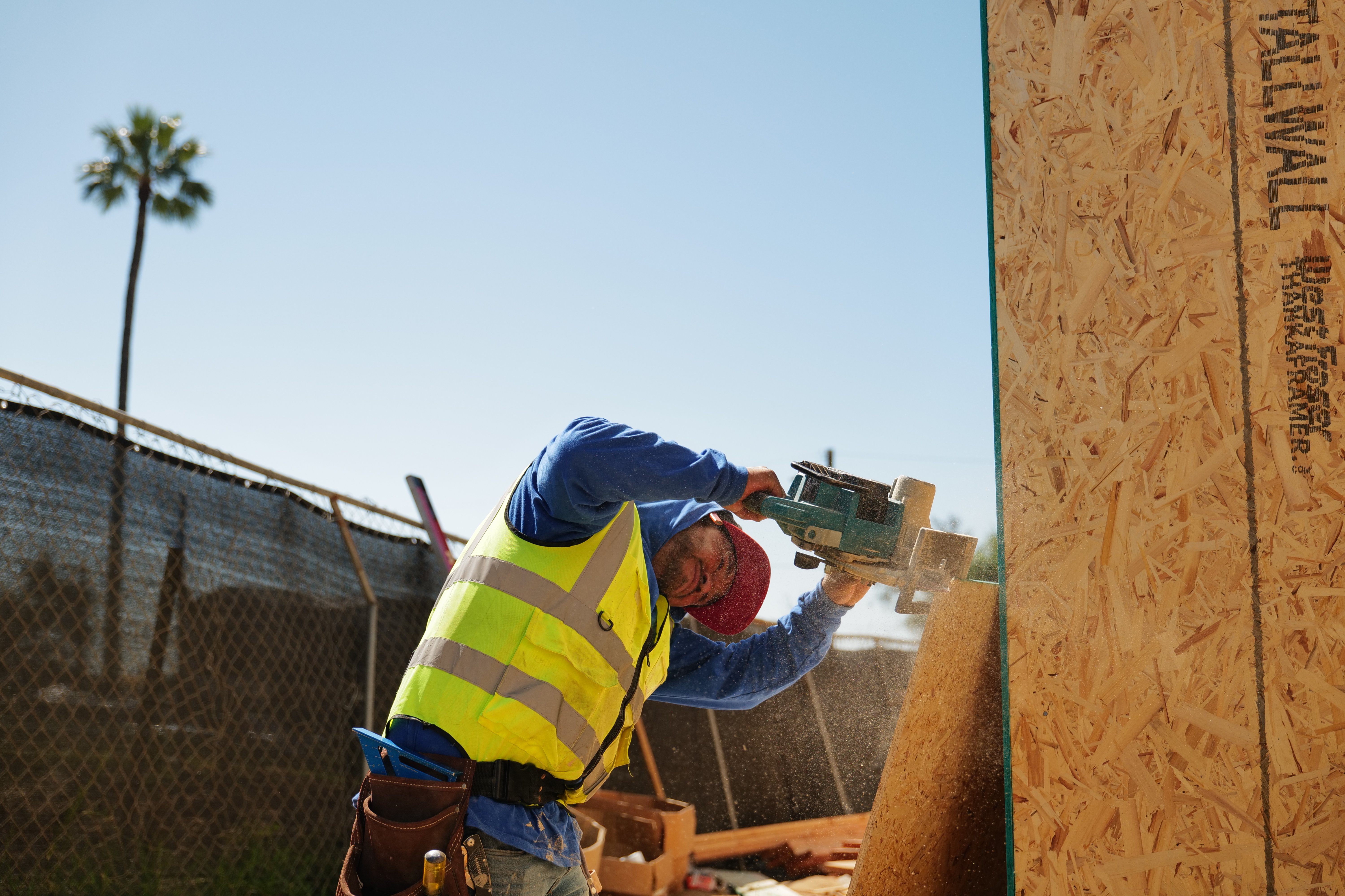 1st Choice crew member cutting wall sheathing on an Altadena rebuild lot under a clear sky