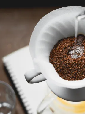 Água quente sendo despejada sobre café moído em um filtro branco para preparo de café coado.