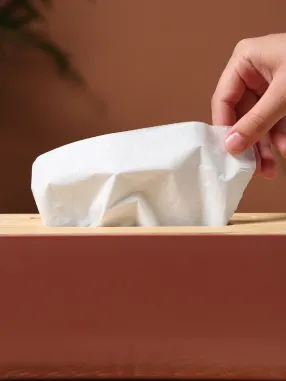 Mão puxando um lenço branco de uma caixa retangular sobre uma superfície de madeira.