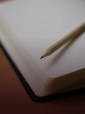 Lápis sobre páginas brancas de um caderno aberto com cantos arredondados.