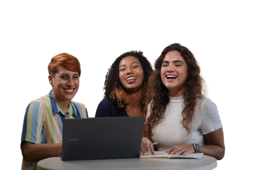 Três mulheres sorrindo enquanto trabalham juntas em um laptop em uma mesa redonda.