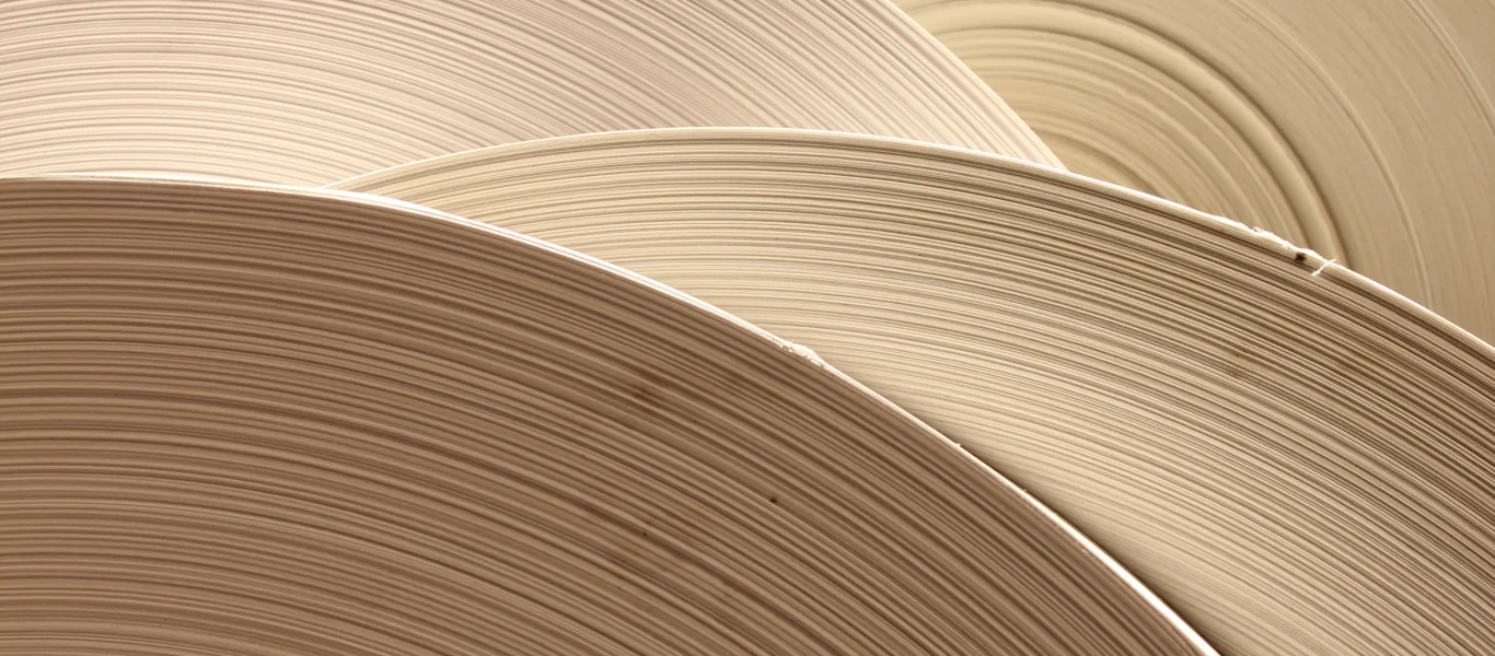 Rolos grandes de papel bege empilhados, mostrando as camadas finas e curvadas do papel.