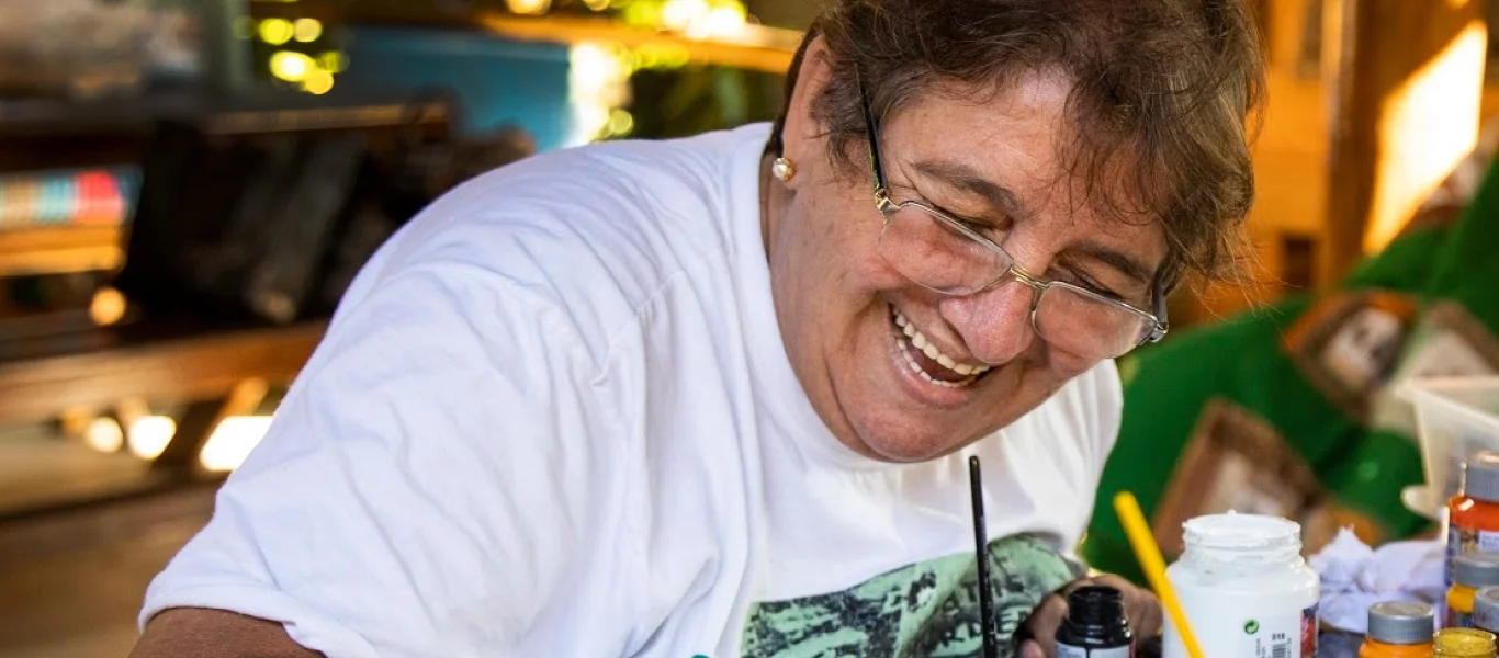 Mulher sorridente pintando com pincel em uma mesa com potes de tinta.