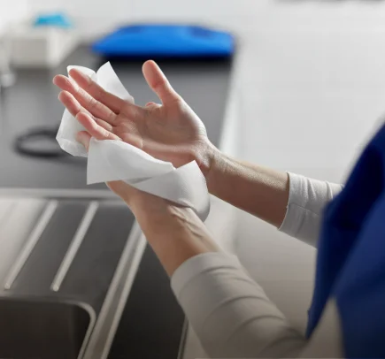 Pessoa secando as mãos com uma toalha de papel próxima a uma pia.