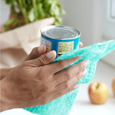 Mãos segurando uma lata enquanto a limpam com um pano azul reutilizável.