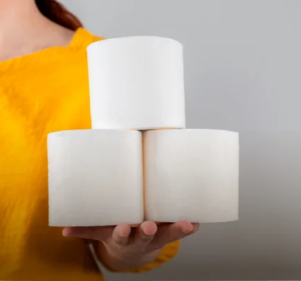 Pessoa vestindo camiseta amarela segurando três rolos de papel higiênico branco empilhados.