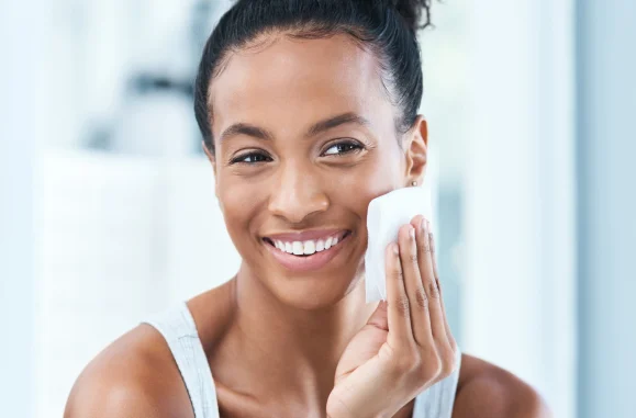 Mulher sorrindo usando um lenço de papel para limpar o rosto em um ambiente claro.