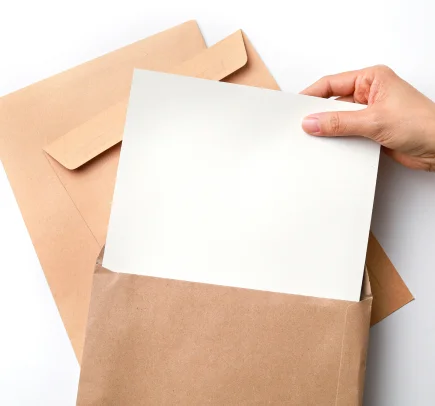 Mão inserindo uma folha de papel branca em um envelope marrom sobre um fundo branco.